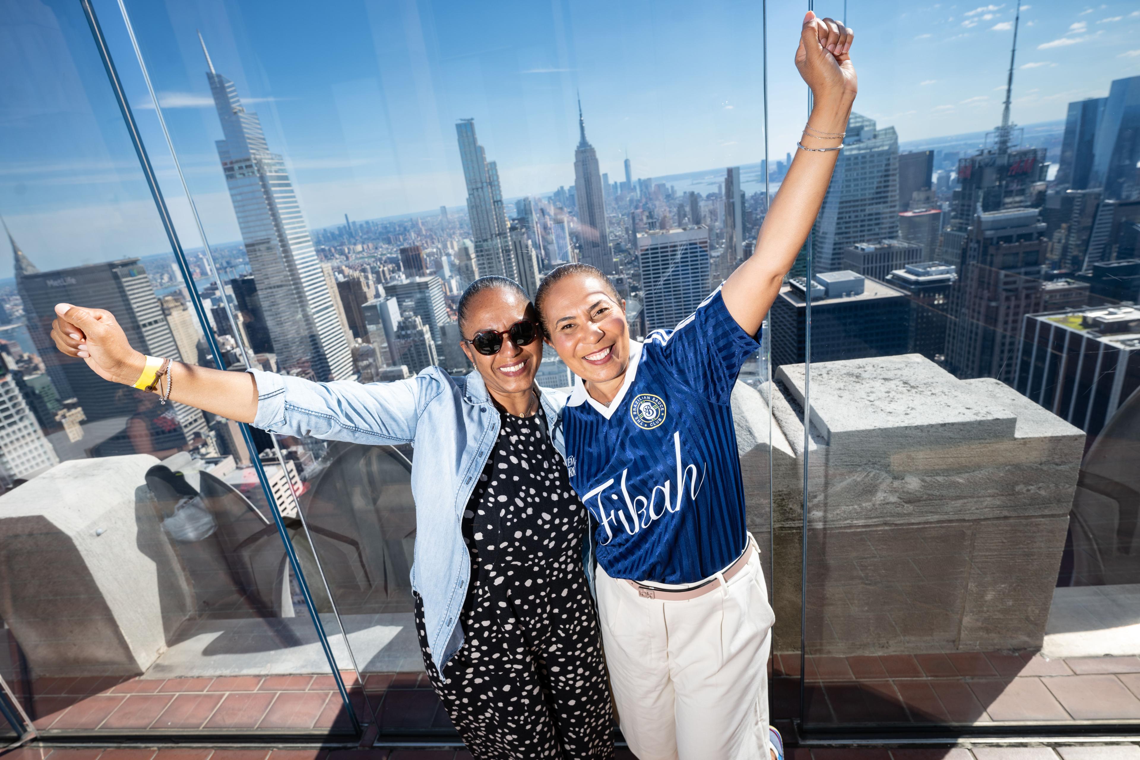 two women smiling at top of the rock in soccer gear