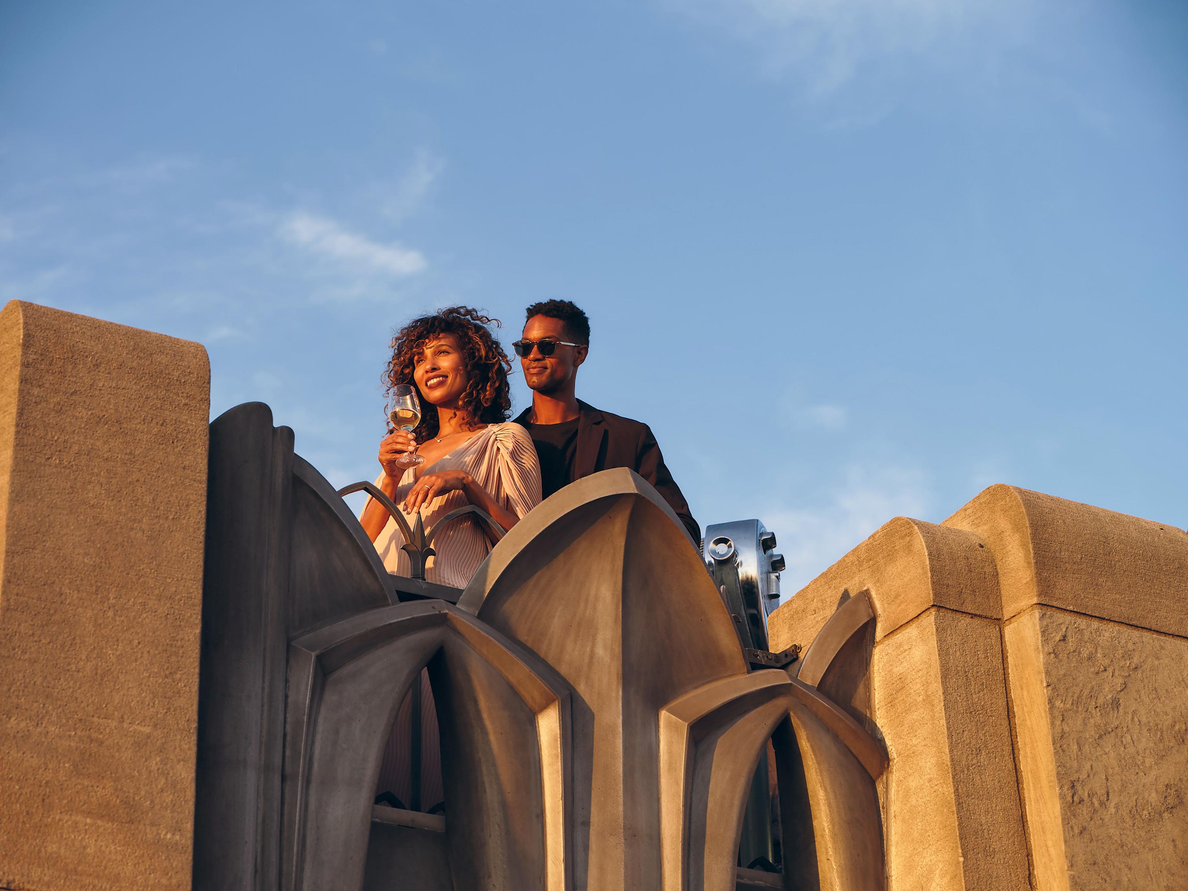 a couple smiling looking out at the sunset holding a wine glass