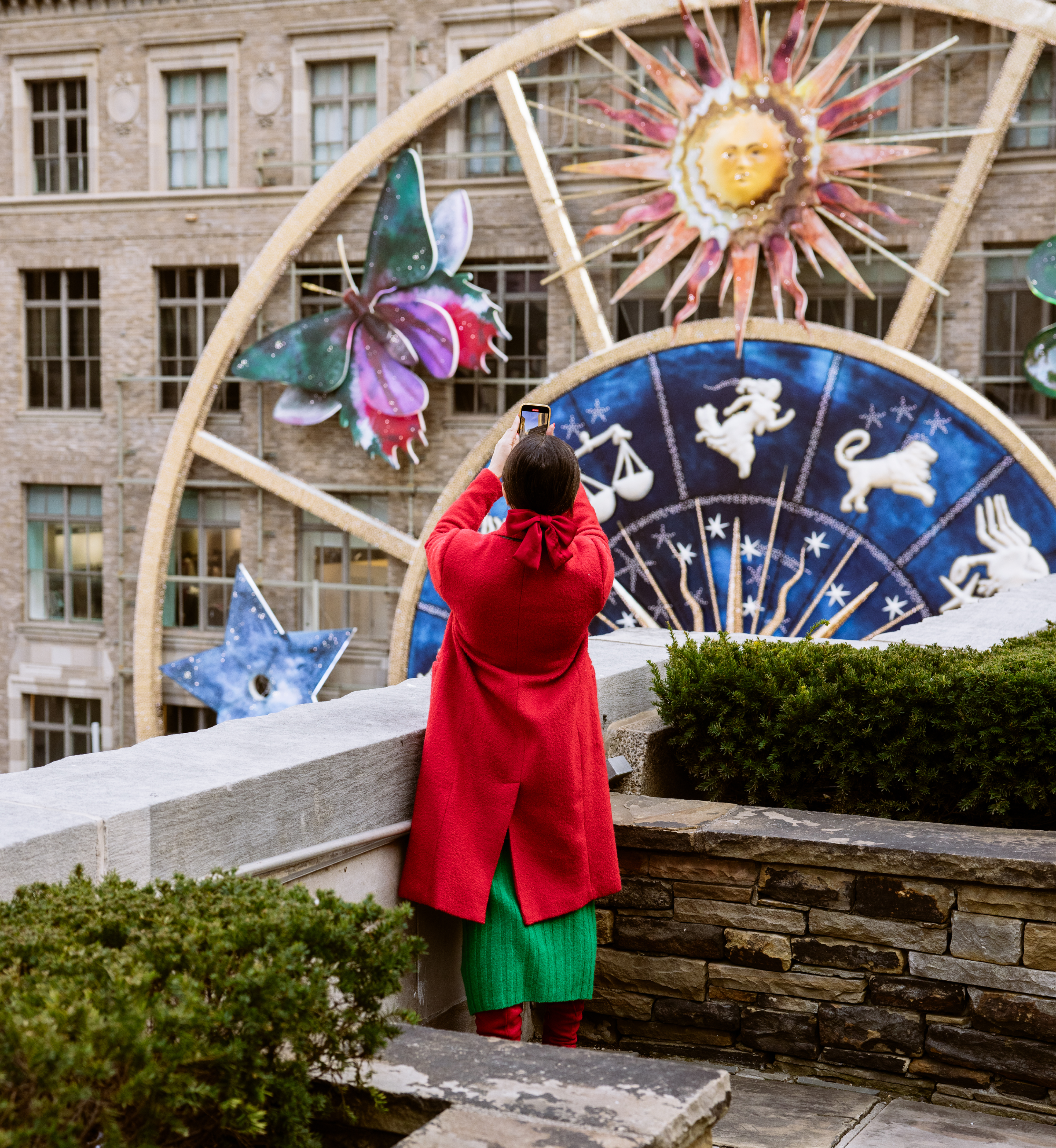 A woman taking a photo of Saks Fifth Avenue's holiday display from a Rockefeller Center rooftop