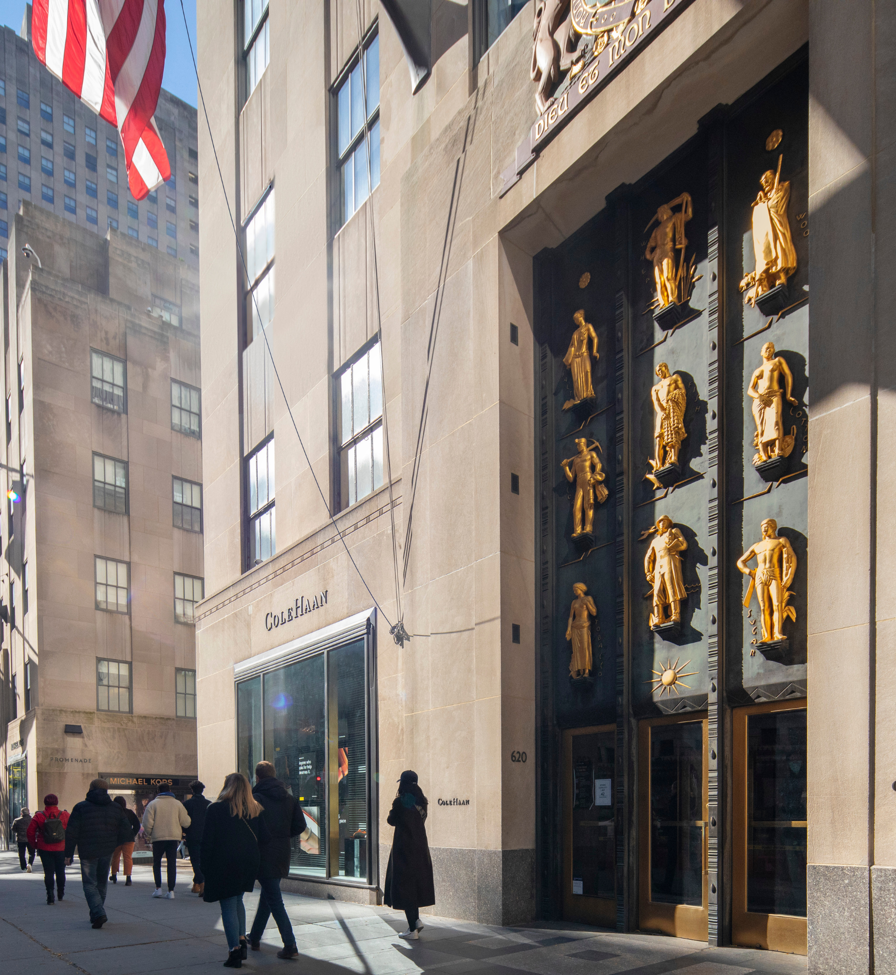 People walking on the street past the Industries of the British Empire art at the entrance of 620 fifth avenue